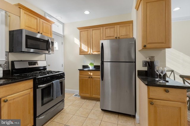 kitchen featuring appliances with stainless steel finishes, light tile patterned floors, and dark stone counters