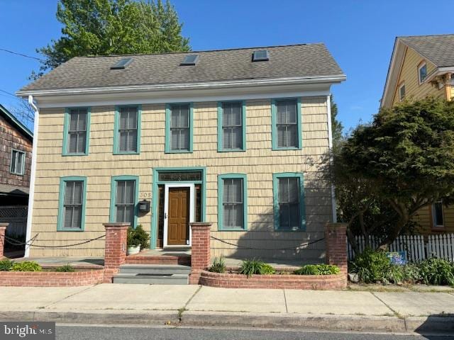 colonial inspired home featuring roof with shingles and fence