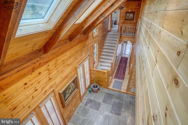 unfurnished living room featuring stone finish flooring, wood walls, and a skylight