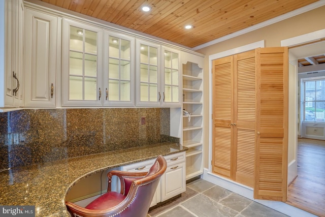 interior space with dark stone counters, built in study area, glass insert cabinets, and white cabinets