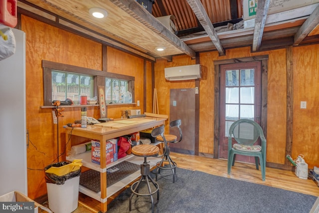 dining room featuring an AC wall unit, wood walls, beam ceiling, and wood finished floors