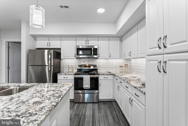 kitchen with tasteful backsplash, stainless steel appliances, white cabinetry, and hanging light fixtures