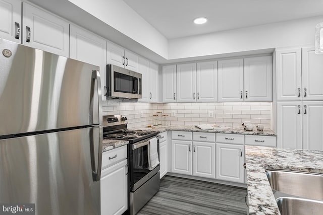 kitchen with light stone countertops, backsplash, stainless steel appliances, dark wood-type flooring, and white cabinetry