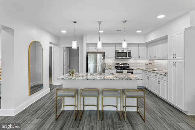 kitchen featuring light stone counters, appliances with stainless steel finishes, white cabinets, backsplash, and decorative light fixtures