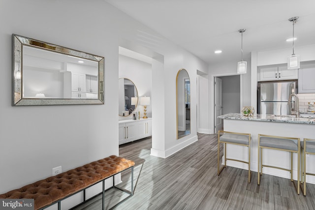 kitchen featuring light stone counters, a kitchen bar, stainless steel refrigerator, white cabinetry, and hanging light fixtures