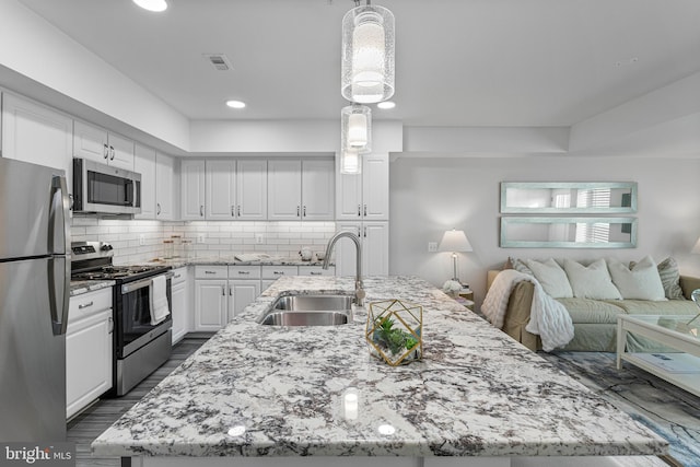 kitchen featuring decorative light fixtures, white cabinetry, stainless steel appliances, a center island with sink, and sink