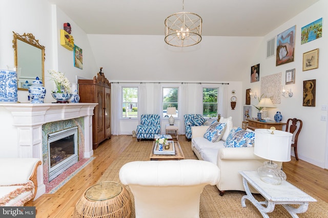 living room featuring an inviting chandelier, a fireplace, a high ceiling, and light wood-type flooring