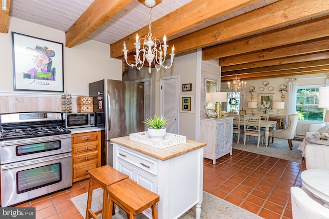 kitchen featuring beamed ceiling, light tile flooring, stainless steel appliances, and an inviting chandelier