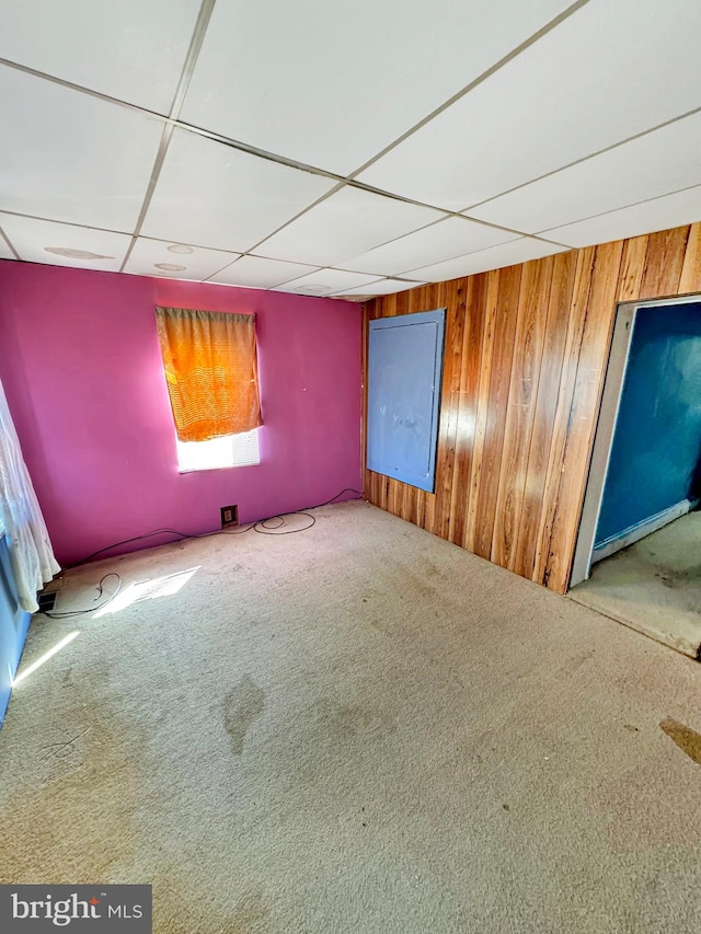 empty room featuring wooden walls, carpet floors, and a drop ceiling