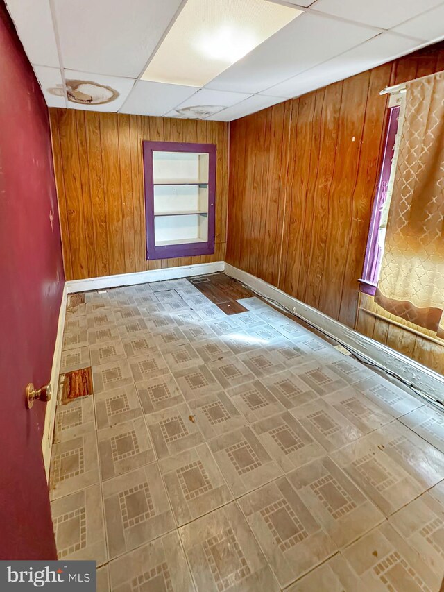 unfurnished room with a healthy amount of sunlight, a paneled ceiling, and wooden walls