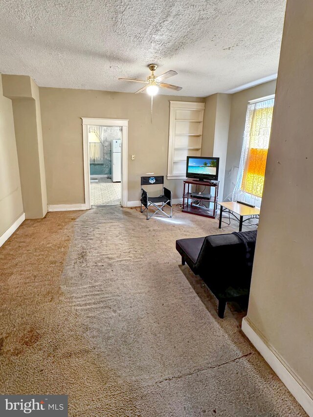 carpeted living room with ceiling fan and a textured ceiling