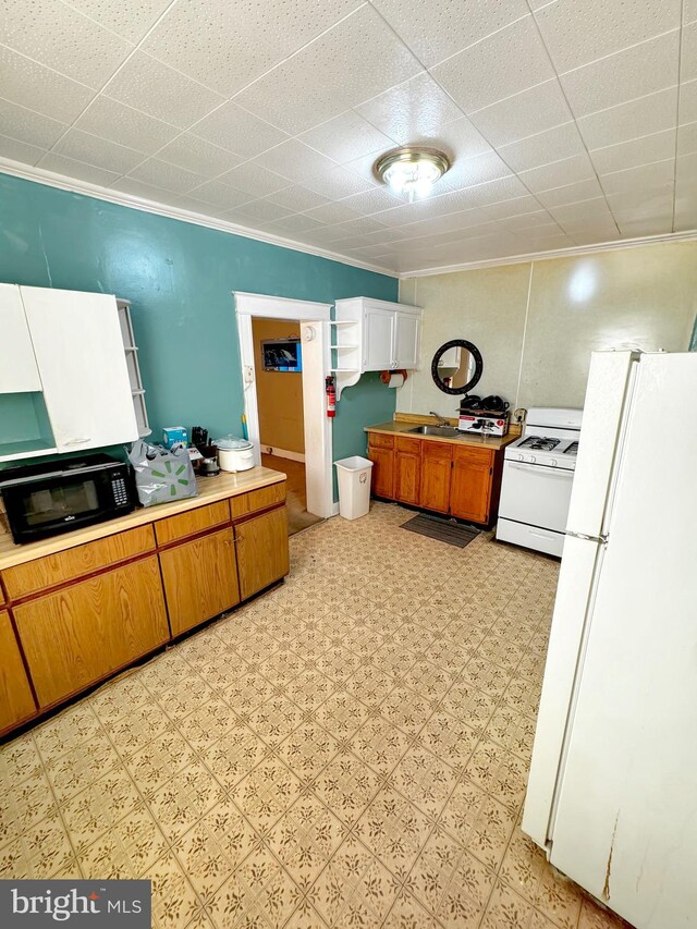 kitchen with white appliances, sink, crown molding, and light tile floors