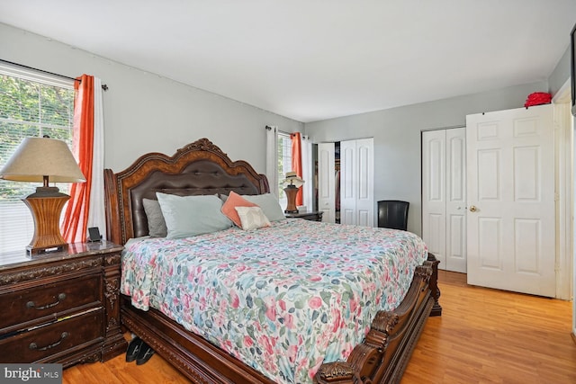 bedroom with two closets and light hardwood / wood-style flooring