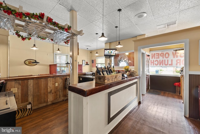 kitchen with a drop ceiling, a wealth of natural light, dark wood-type flooring, and decorative light fixtures