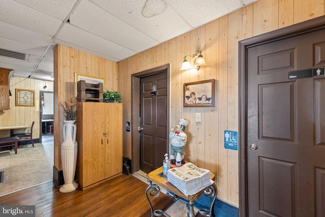 entryway featuring dark hardwood / wood-style flooring, wood walls, and a drop ceiling