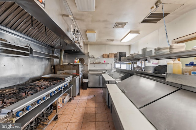 kitchen featuring stainless steel counters, wall chimney range hood, and light tile flooring