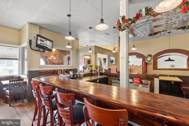 bar featuring hanging light fixtures, hardwood / wood-style flooring, and a paneled ceiling