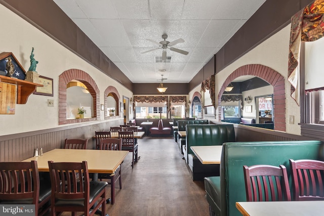 dining area with a drop ceiling, dark wood-type flooring, brick wall, and ceiling fan