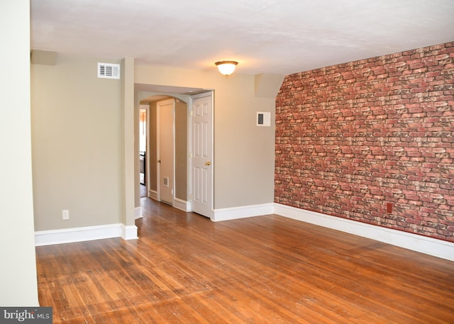 spare room with hardwood / wood-style floors and brick wall