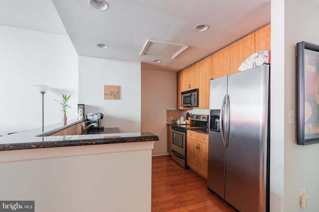 kitchen featuring kitchen peninsula, hardwood / wood-style floors, backsplash, appliances with stainless steel finishes, and dark stone countertops