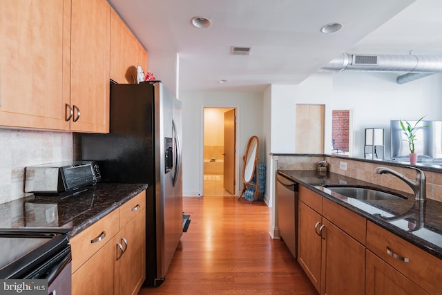 kitchen with dark stone countertops, appliances with stainless steel finishes, sink, and light hardwood / wood-style flooring