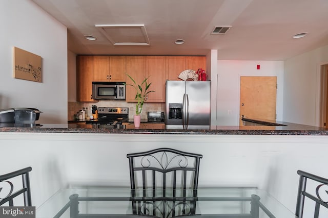 kitchen featuring dark stone countertops, kitchen peninsula, decorative backsplash, and stainless steel appliances