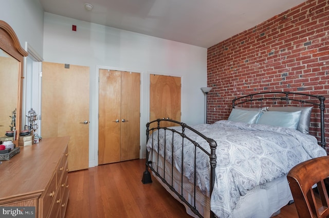 bedroom with hardwood / wood-style floors, brick wall, and two closets