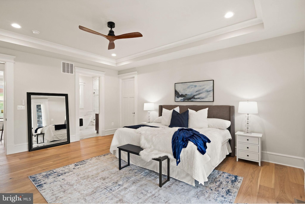 bedroom with ensuite bathroom, ceiling fan, a tray ceiling, and hardwood / wood-style flooring