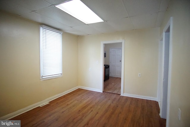 empty room with a healthy amount of sunlight, wood-type flooring, and a drop ceiling