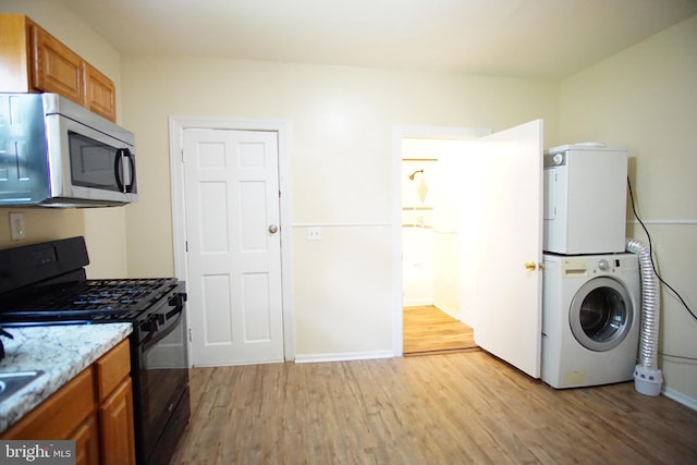 kitchen with light wood-type flooring, stacked washer and dryer, black gas range oven, and light stone counters