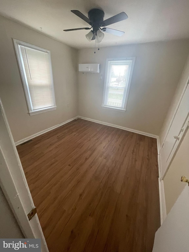 empty room with a wall mounted air conditioner, dark hardwood / wood-style flooring, and ceiling fan