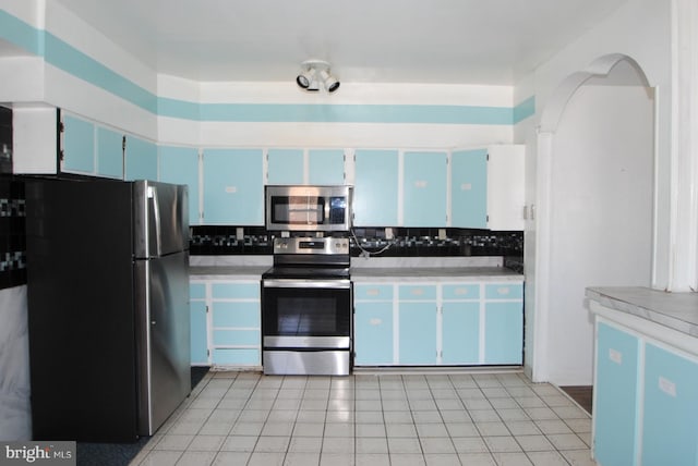 kitchen with stainless steel appliances, light tile patterned flooring, tasteful backsplash, and blue cabinetry