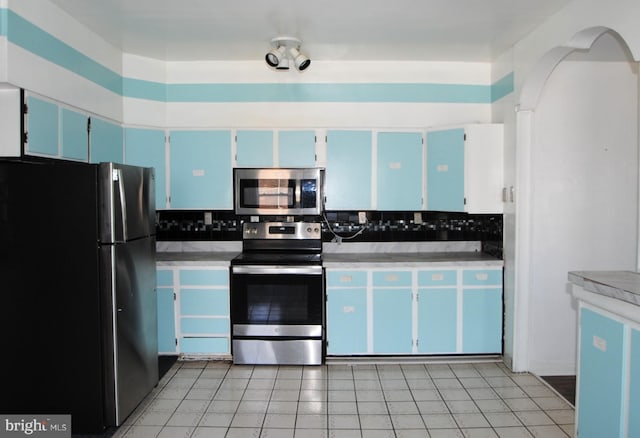 kitchen with blue cabinetry, appliances with stainless steel finishes, light tile patterned floors, and decorative backsplash