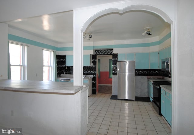 kitchen featuring blue cabinets, light tile patterned floors, stainless steel appliances, and kitchen peninsula