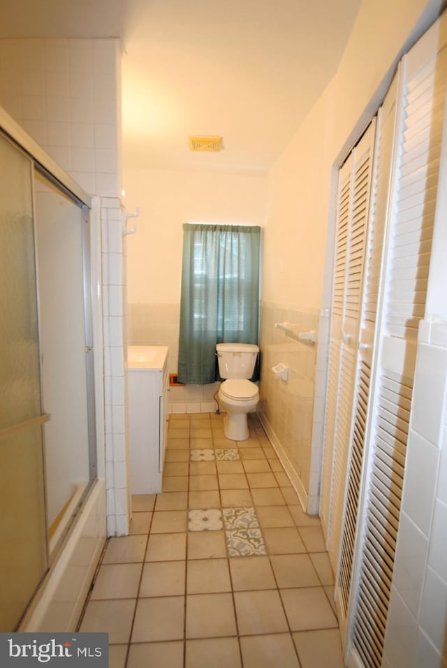 full bathroom featuring tile patterned flooring, toilet, tile walls, bath / shower combo with glass door, and vanity