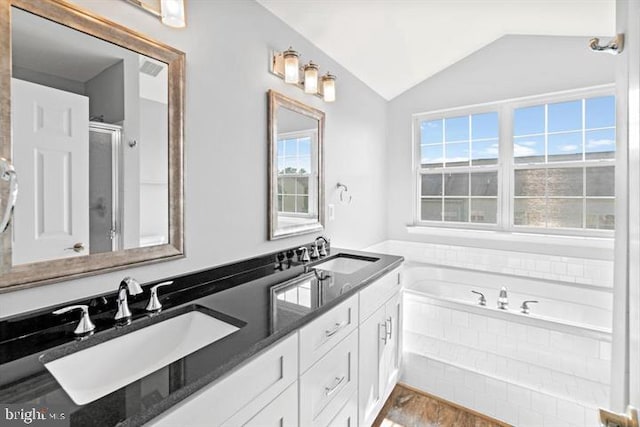 bathroom featuring double sink, large vanity, a relaxing tiled bath, and lofted ceiling