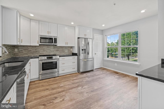 kitchen with dark stone counters, appliances with stainless steel finishes, light hardwood / wood-style floors, and sink