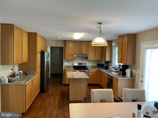 kitchen featuring stainless steel appliances, dark hardwood / wood-style flooring, light stone counters, pendant lighting, and a center island