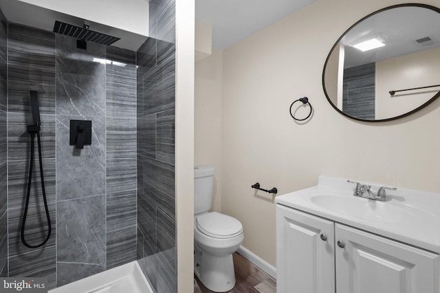 bathroom with toilet, vanity, a tile shower, and wood-type flooring