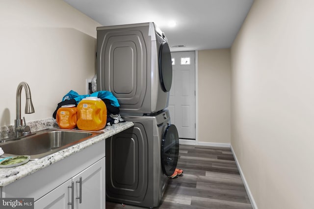 laundry area with sink, dark wood-type flooring, stacked washer and clothes dryer, and cabinets