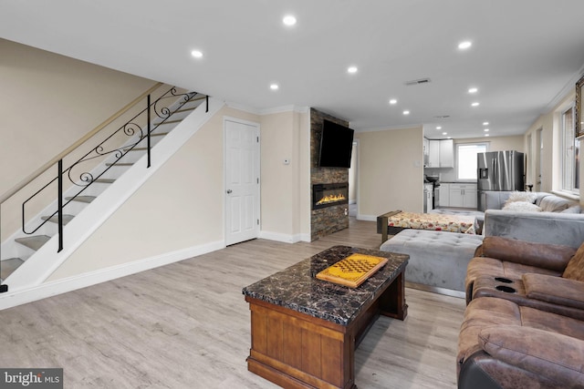 living room with light hardwood / wood-style floors, ornamental molding, and a stone fireplace