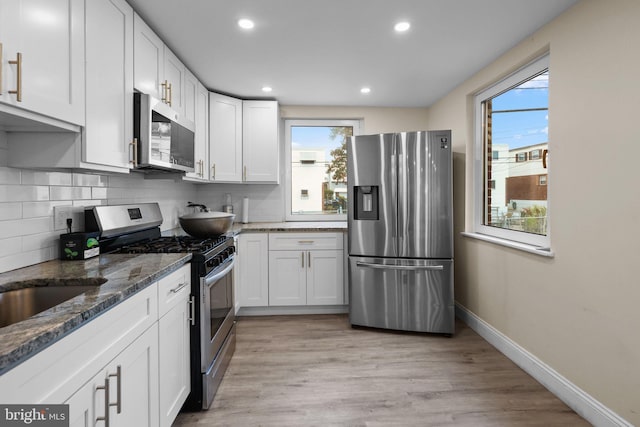 kitchen with a healthy amount of sunlight, appliances with stainless steel finishes, white cabinets, and light hardwood / wood-style floors