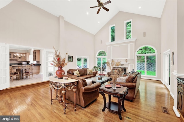 living room featuring ceiling fan with notable chandelier, high vaulted ceiling, and light wood-type flooring