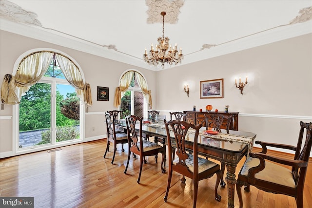 dining area with light hardwood / wood-style flooring, a wealth of natural light, an inviting chandelier, and ornamental molding