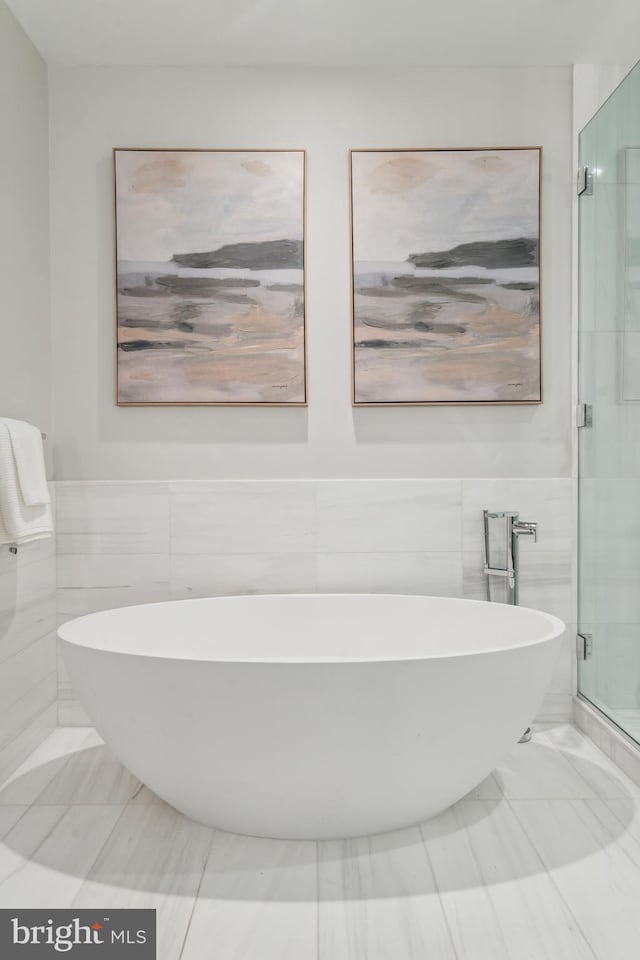 full bathroom with a shower stall, tile walls, a freestanding bath, and wainscoting