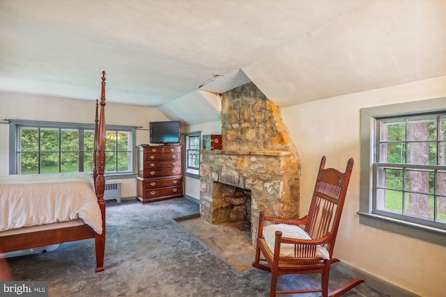 carpeted bedroom with vaulted ceiling, a stone fireplace, and radiator