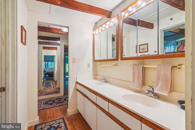 bathroom with large vanity, hardwood / wood-style flooring, beam ceiling, and dual sinks