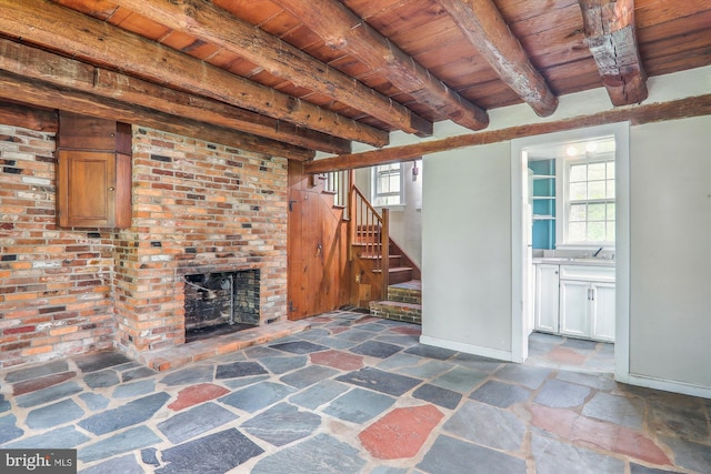 unfurnished living room featuring a brick fireplace, brick wall, beamed ceiling, wood ceiling, and dark tile floors