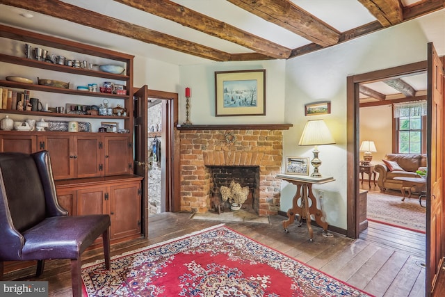 living area with beamed ceiling, a fireplace, and hardwood / wood-style flooring