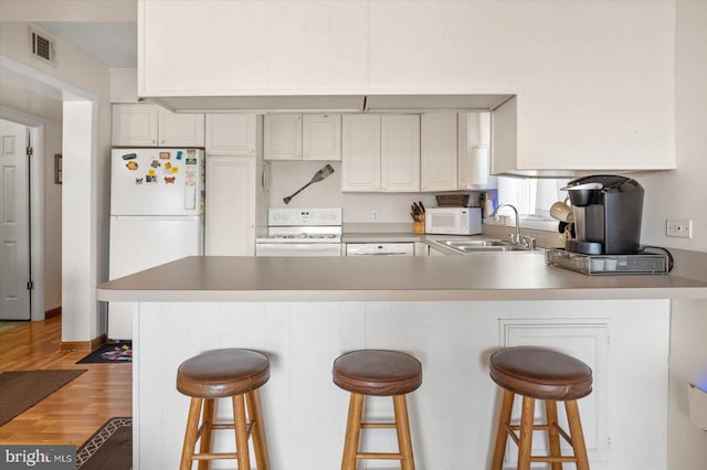 kitchen featuring white appliances, visible vents, a peninsula, a sink, and light wood-style floors